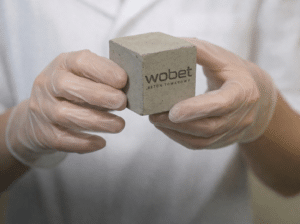 Próbka betonu towarowego Wobet w kształcie sześcianu trzymana w rękach w rękawiczkach w laboratorium